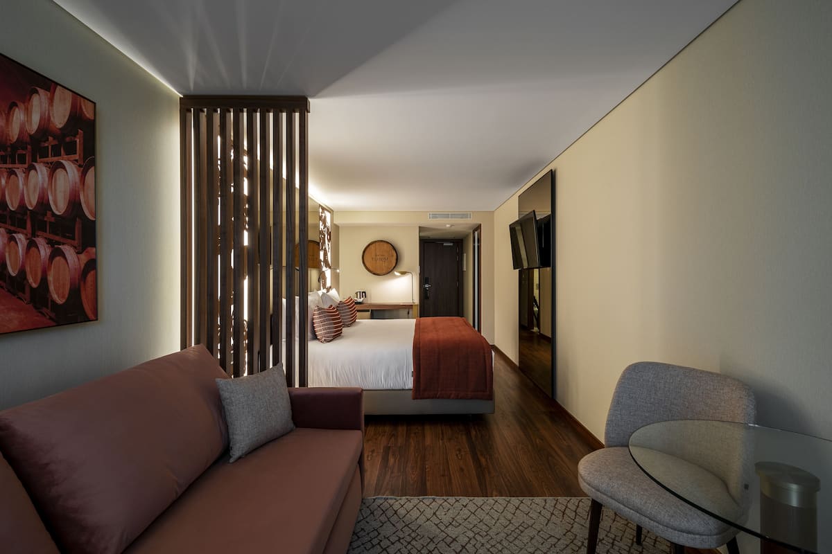 Una habitación de hotel moderna con una cama, un sofá, una mesa de vidrio y un televisor.