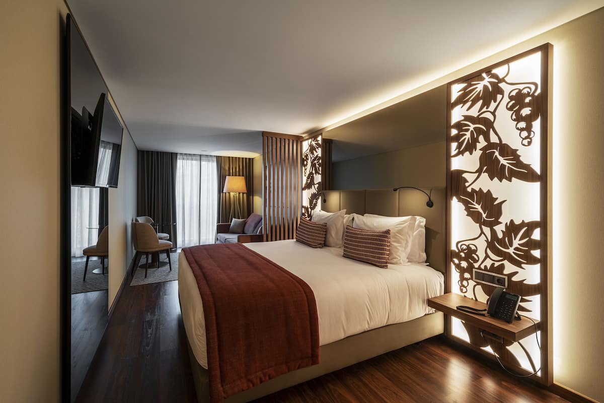 Habitación de hotel con cama, mesita de noche, lámpara y un separador decorativo.