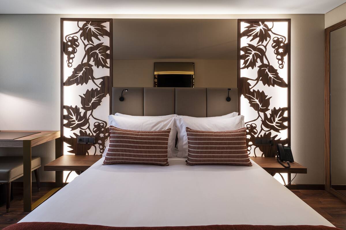 Habitación de hotel con una cama grande, dos mesitas de noche, un escritorio y un panel decorativo con diseños de parra.