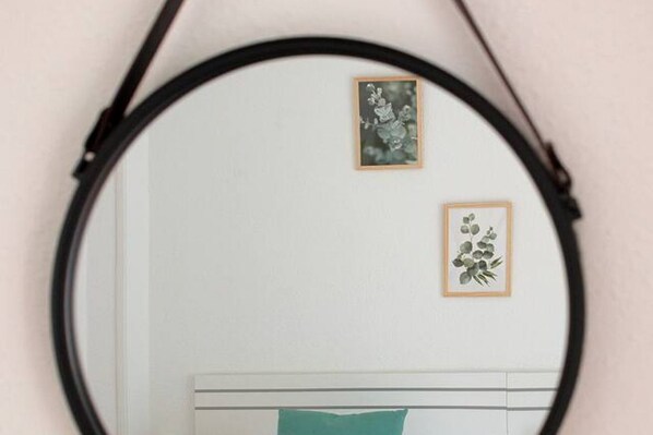 A round mirror with a black frame, reflecting two framed pictures on a wall.