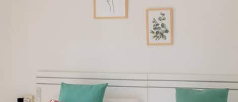 A hotel room with a bed, pillows, and two framed botanical prints on the wall.