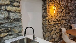 A kitchen with a modern sink, stone wall, and hanging light fixtures.