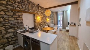 A compact kitchen with a stone wall, a washing machine, and a dining area with a round table and chairs.