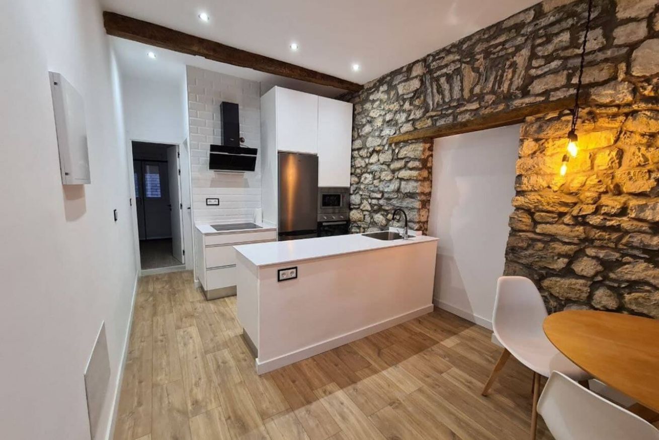 A modern kitchen with white cabinetry, a stone accent wall, and a wooden dining table.