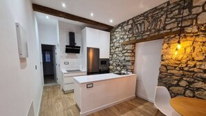 A modern kitchen with white cabinetry, a stone accent wall, and a wooden dining table.