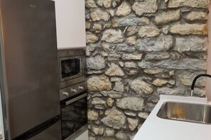 Una cocina con pared de piedra, refrigerador de acero inoxidable, horno y lavamanos.