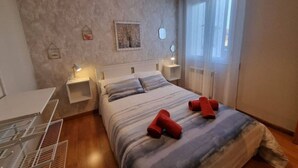 A bedroom with a bed, bedside tables, a hanging light fixture, and a window with curtains.