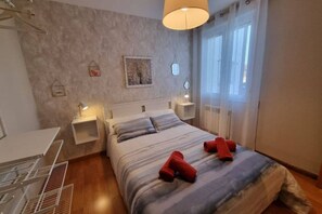 Een slaapkamer met een bed, nachtkastjes, een hanglamp en een raam met gordijnen.