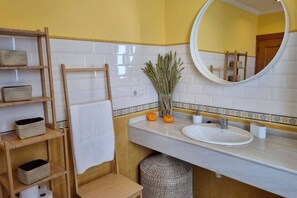 Een badkamer met een witte wastafel, een spiegel, een handdoekhouder en planken met manden.