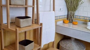 Een badkamer met een houten plank, een witte handdoek, een vaas met gedroogde planten en twee pompoenen op het aanrecht.
