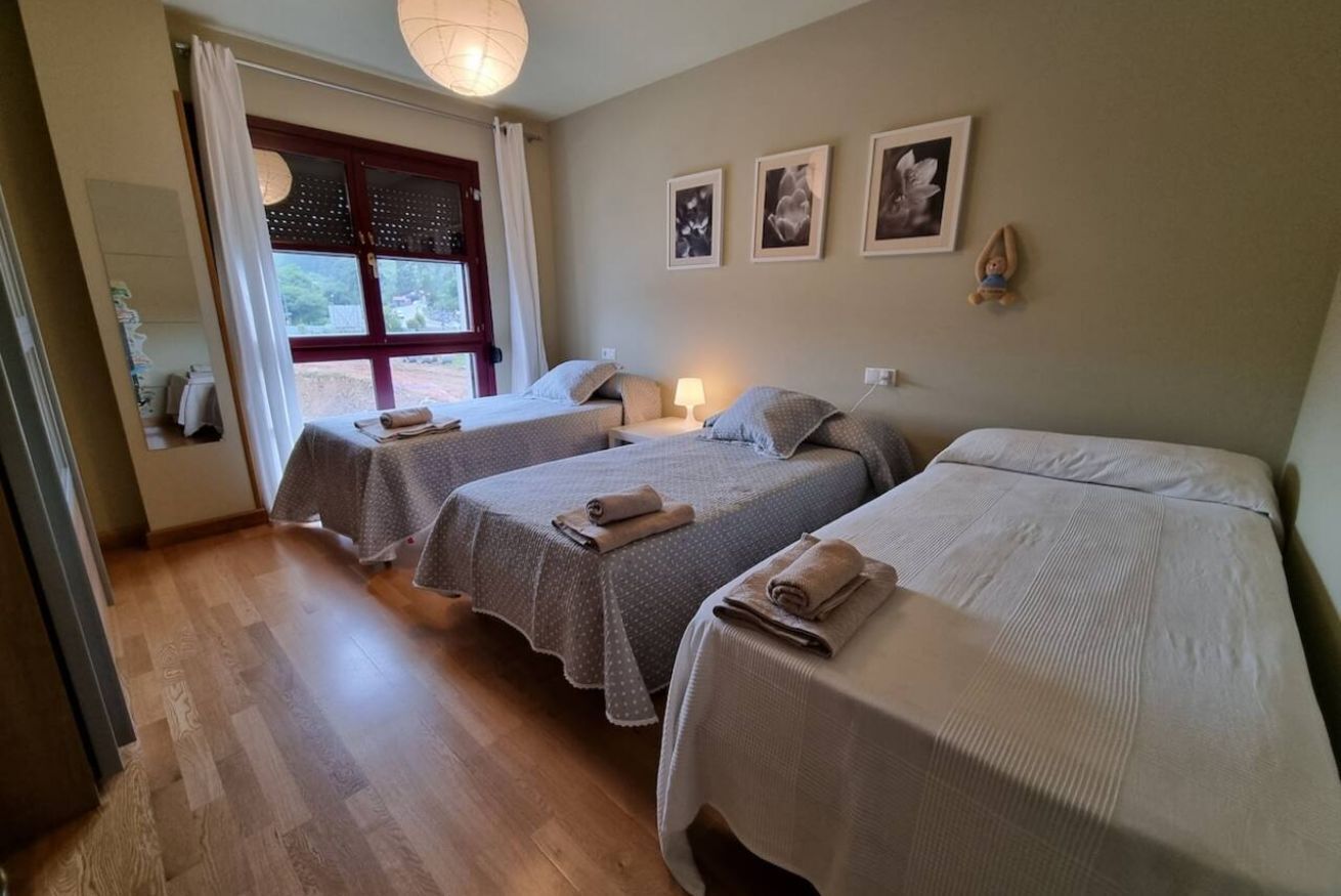 Una habitación con dos camas, una ventana con cortinas, un muro con cuadros enmarcados y piso de madera.