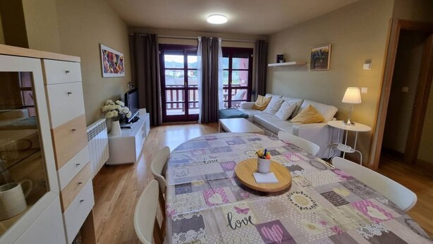 A cozy living room with a sofa, a dining table with a placemat, and a kitchen area with cabinets and a refrigerator.