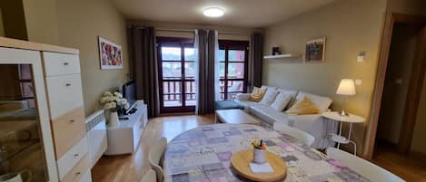 Una sala de estar acogedora con un sofá, una mesa de comedor con un mantel individual y una zona de cocina con armarios y un refrigerador.