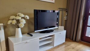 A white TV stand with a flat-screen TV, a remote control, and a vase of white flowers.