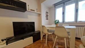 Ein modernes Wohnzimmer mit Flachbildfernseher, einem Esstisch mit Stühlen und einer Topfpflanze.