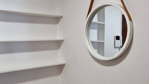 Eine weiße Wand mit einem runden Spiegel und drei weißen Regalen.