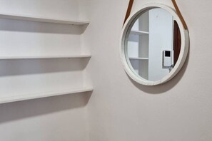 Una pared blanca con un espejo redondo y tres estantes blancos.