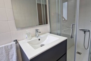 Un baño con lavamanos blanco, espejo y cabina de ducha de vidrio.