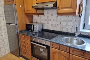 Una cocina con armarios de madera, un lavamanos de acero inoxidable, un microondas, una estufa y un refrigerador.