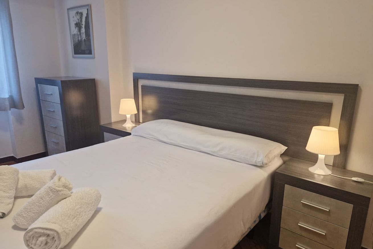 Ett hotellrum med en säng, två sänglampor, ett nattduksbord, en byrå och två hoprullade handdukar.