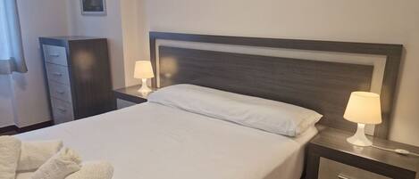 Ett hotellrum med en säng, två sänglampor, ett nattduksbord, en byrå och två hoprullade handdukar.