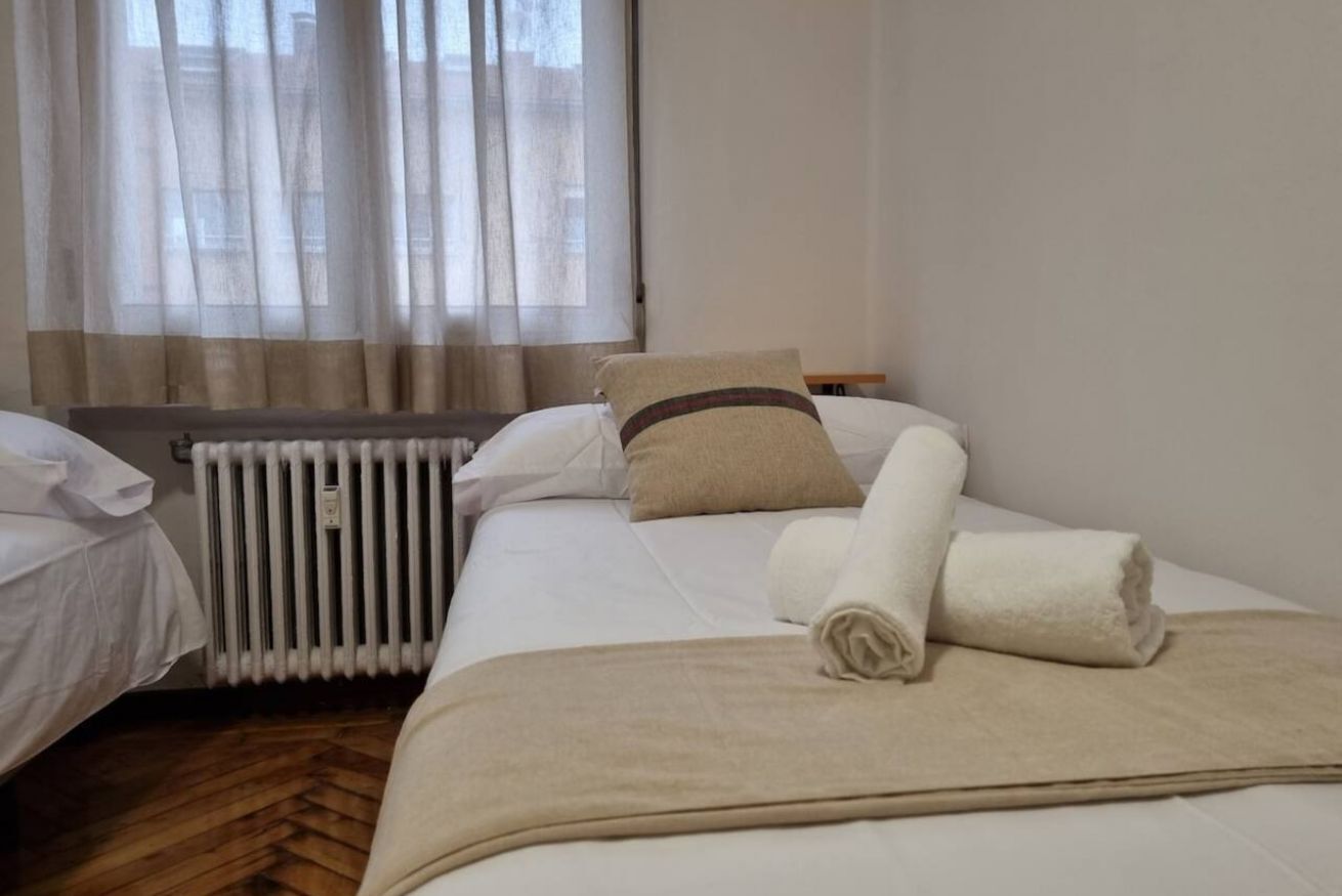 A hotel room with a bed, a radiator, and a window with curtains.