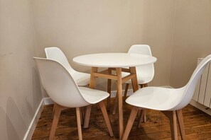 A small, round wooden table with four white chairs. The room has wooden flooring and white walls.