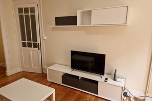 Una habitación con una televisión sobre un soporte blanco, una puerta con paneles de vidrio y una mesa blanca.