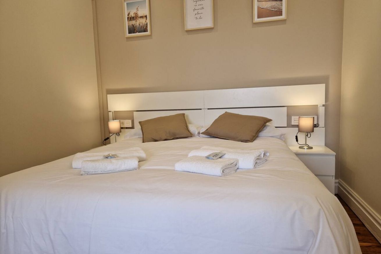 A neatly made bed with white linens and brown pillows, two bedside lamps, and a framed quote on the wall.