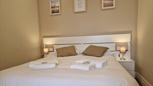 Un lit bien fait, avec du linge de lit blanc et des oreillers marron, deux lampes de chevet et une citation encadrée accrochée au mur.
