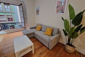 Una sala de estar con un sofá gris, dos cojines amarillos, una mesa de centro blanca y una planta grande en maceta.