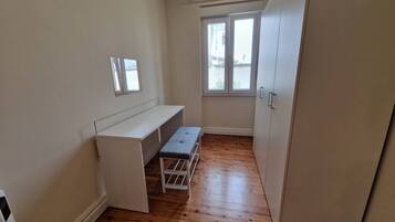 Una habitación pequeña con un escritorio blanco, un banco, una ventana y un armario.