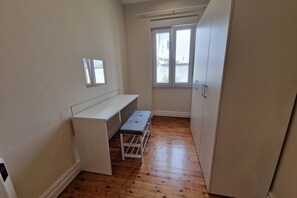 Una habitación pequeña con un escritorio blanco, un banco, una ventana y un armario.