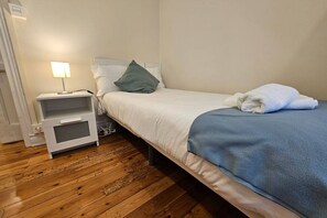 Un dormitorio con una cama, una mesita de noche, una lámpara y una manta azul.
