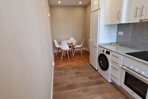 Una cocina funcional con lavadora, una mesa de comedor con sillas y armarios blancos.