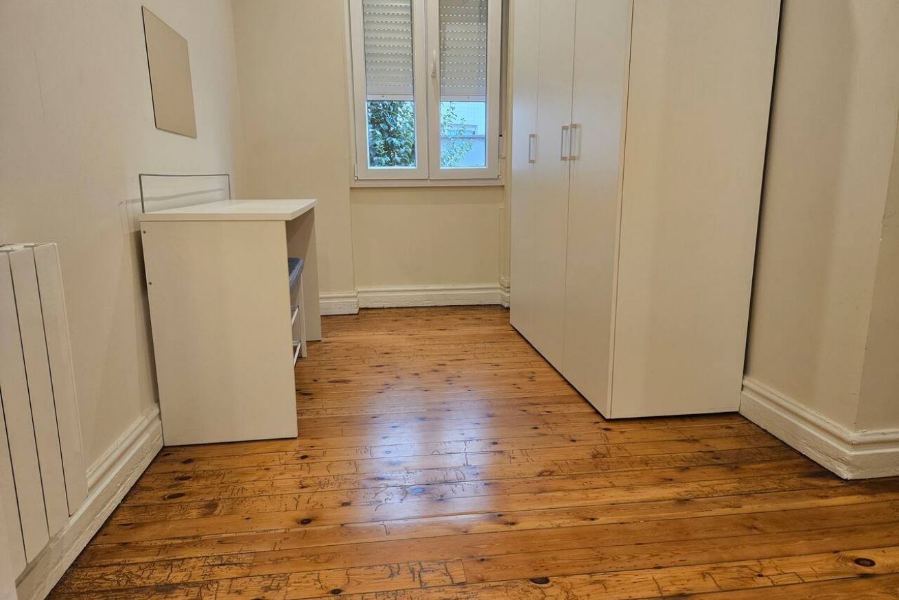 A narrow room with a wooden floor, white walls, a window with blinds, and a white cabinet.