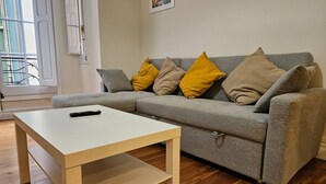 Un salon avec un canapé gris, des coussins jaunes et beiges, une table basse blanche et un parquet en bois.