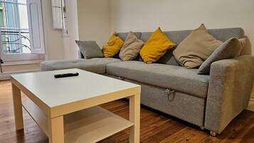 A living room with a grey sofa, yellow and beige cushions, a white coffee table, and wooden flooring.