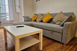 Ein Wohnzimmer mit grauem Sofa, gelb-beigen Kissen, einem weißen Couchtisch und Holzböden.