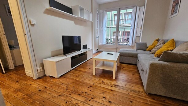Un salon avec un téléviseur, un canapé et un plancher en bois.