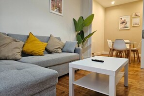 Una sala moderna con un sofá gris, una mesa de centro blanca y un comedor con una mesa y sillas blancas.