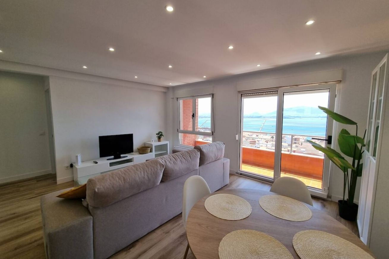 A modern living room with a sofa, TV, and dining area with a balcony view.