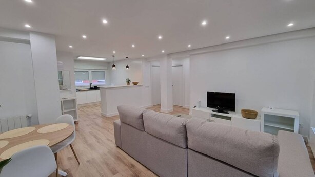 A modern living room with a sofa, a dining table, and a TV. - C01A01 Apartamento Moderno con vistas al mar (Santander)