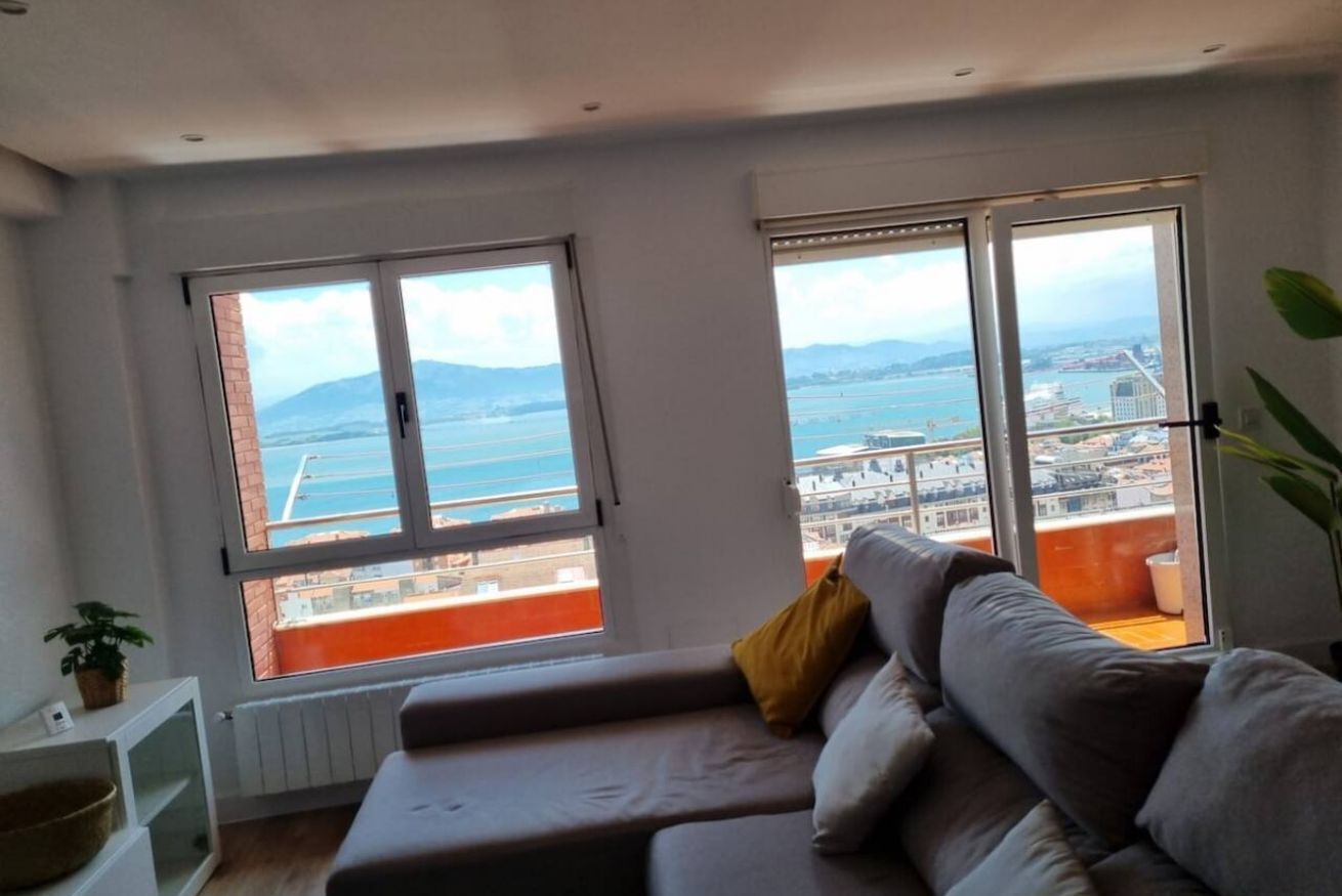 Una sala moderna con sofá, ventanas amplias y vista al mar.
