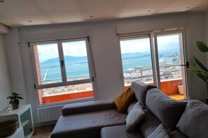 A modern living room with a sofa, large windows, and a view of the sea. - C01A01 Apartamento Moderno con vistas al mar (Santander)