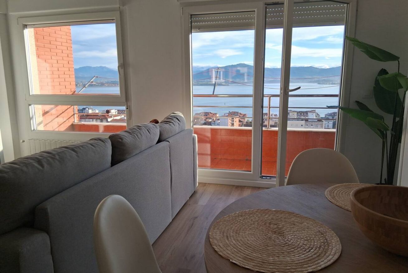 Un saló amb un sofà, una taula de dinar amb cadires, vista d'un pont i una planta.