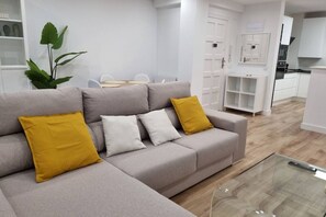 A modern living room with a grey sofa, a glass coffee table, and a dining area in the background. - C01A01 Apartamento Moderno con vistas al mar (Santander)