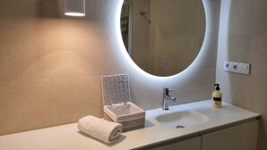 Un baño moderno con un espejo redondo, un lavamanos blanco, una toalla, un dispensador de jabón y una cesta de mimbre.