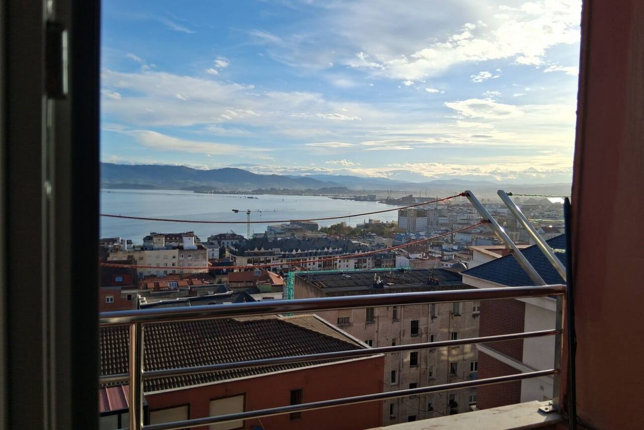 Un paisaje urbano con edificios, un cuerpo de agua y montañas al fondo.