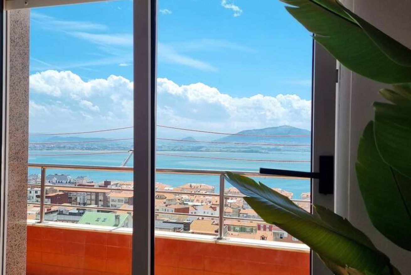 A balcony with a view of a coastal town, a clear sky, and a mountain in the distance.